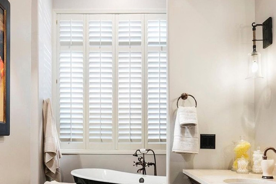 Large window with white Polywood shutters above a bathtub.
