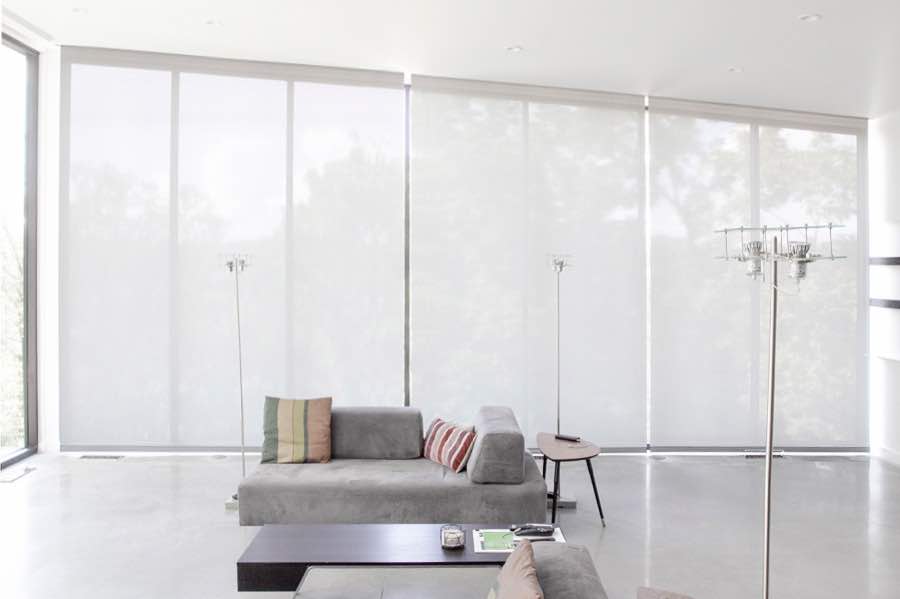 Motorized window shades make controlling natural light effortless in your Sacramento great room. White motorized shades on a wall of tall great room windows