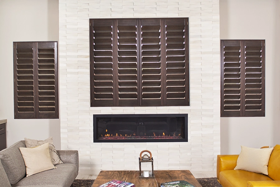 Finding the right window treatment material is essential. These Ovation® wood plantation shutters bring warmth and beauty to this living room. Wood Ovation® shutters in a living room with white walls and a fireplace